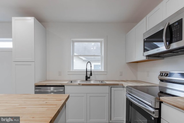 kitchen with white cabinetry, appliances with stainless steel finishes, butcher block counters, and a sink