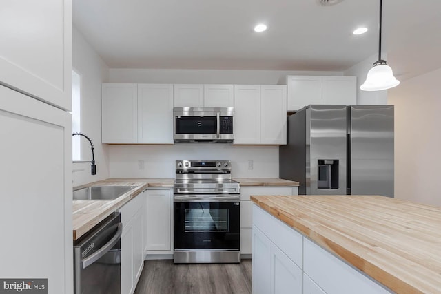 kitchen with a sink, decorative light fixtures, stainless steel appliances, white cabinets, and wooden counters