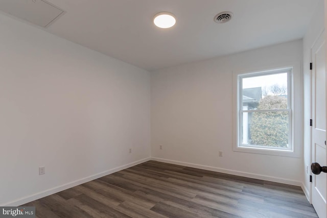 empty room featuring visible vents, dark wood-type flooring, and baseboards