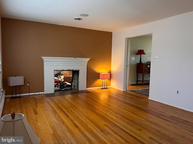 unfurnished living room featuring visible vents, wood finished floors, a baseboard radiator, baseboards, and a brick fireplace