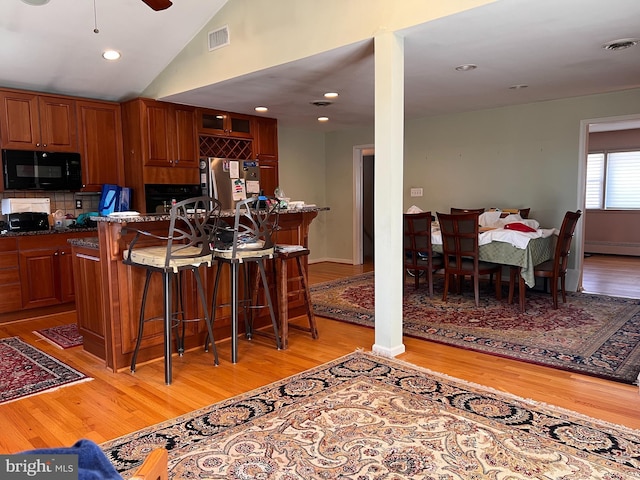 kitchen with visible vents, black microwave, a breakfast bar area, freestanding refrigerator, and light wood-style floors