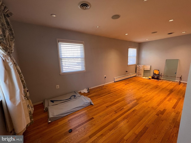 empty room with a baseboard heating unit, baseboards, visible vents, and wood finished floors