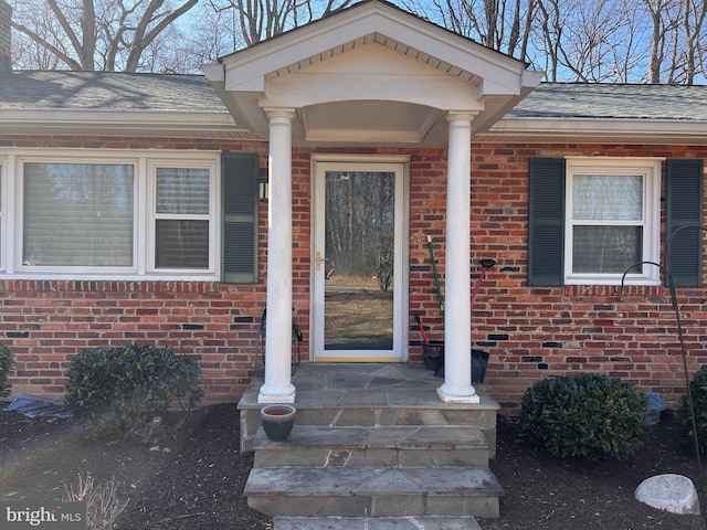 view of exterior entry featuring brick siding and a shingled roof