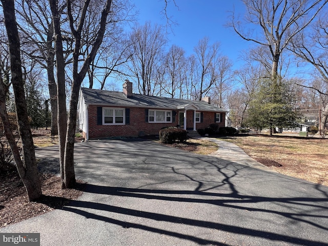 view of front of house with brick siding, driveway, and a chimney