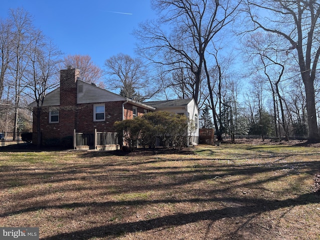 view of side of property with brick siding, a lawn, and a chimney