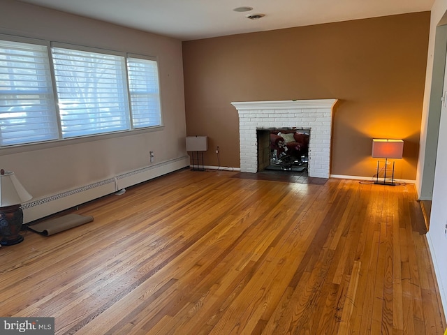 unfurnished living room with baseboards, a baseboard radiator, wood-type flooring, and a brick fireplace