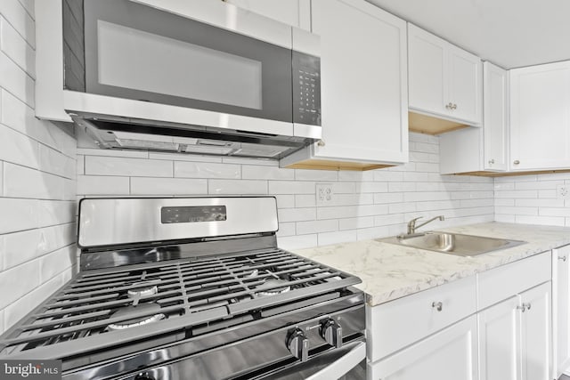 kitchen with a sink, light stone countertops, appliances with stainless steel finishes, and white cabinetry