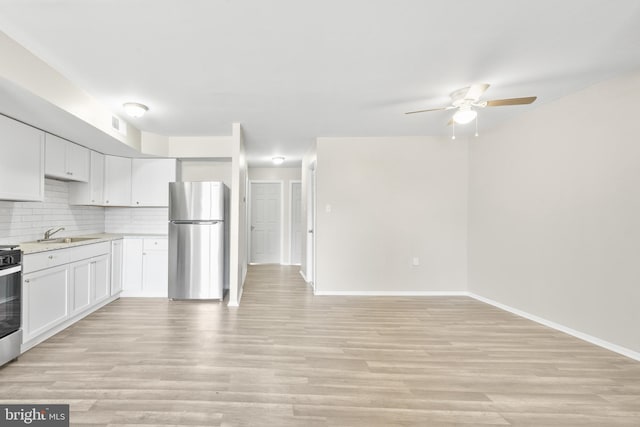 kitchen with light wood-type flooring, light countertops, decorative backsplash, freestanding refrigerator, and a sink