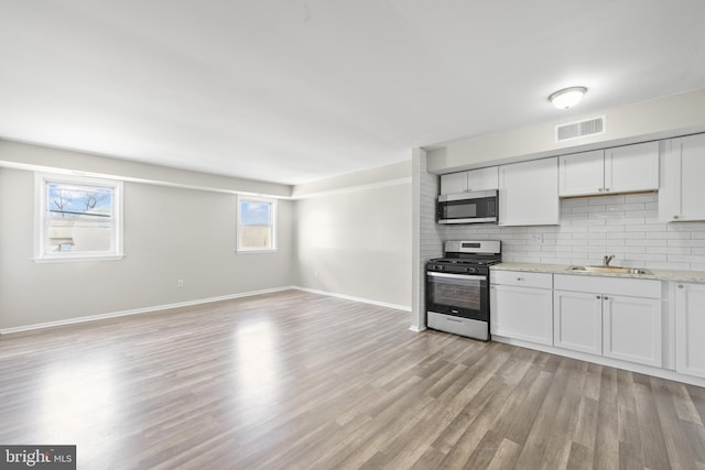 kitchen with visible vents, decorative backsplash, appliances with stainless steel finishes, light wood-style floors, and a sink