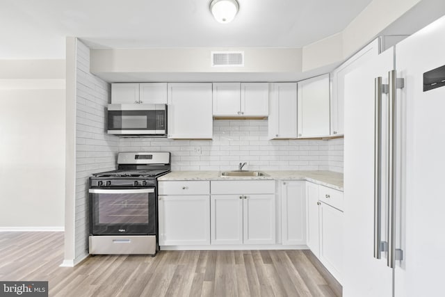 kitchen featuring visible vents, a sink, stainless steel appliances, light wood finished floors, and decorative backsplash