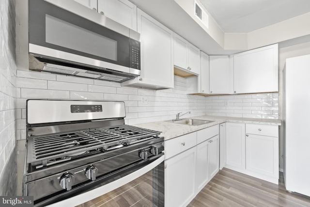 kitchen with visible vents, a sink, decorative backsplash, stainless steel appliances, and white cabinetry