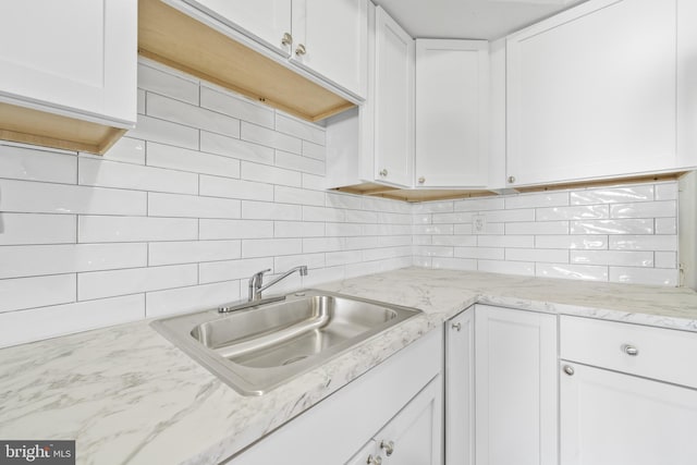 kitchen with a sink, light stone countertops, tasteful backsplash, and white cabinetry