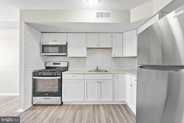 kitchen featuring visible vents, light wood-style flooring, a sink, backsplash, and appliances with stainless steel finishes