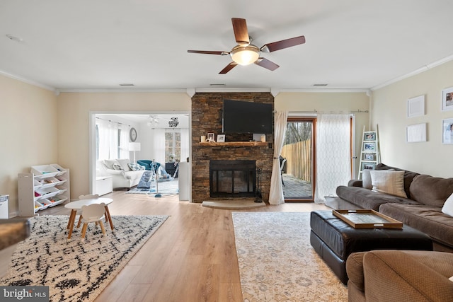 living room with visible vents, ceiling fan, ornamental molding, light wood-style flooring, and a fireplace