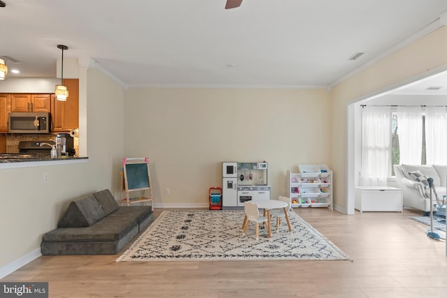 interior space featuring visible vents, ceiling fan, baseboards, ornamental molding, and wood finished floors