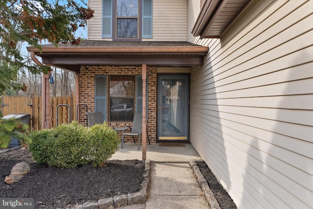 view of exterior entry featuring fence and brick siding