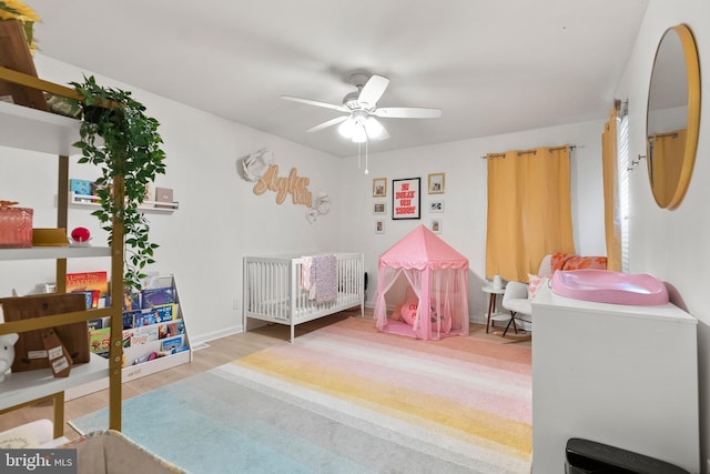 bedroom with ceiling fan, a nursery area, and wood finished floors