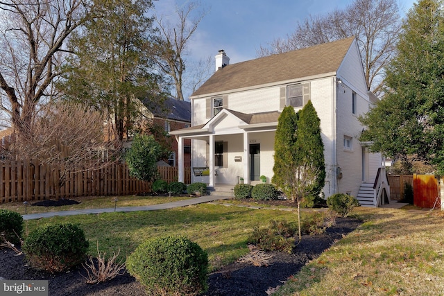 view of front facade featuring brick siding, fence, a front yard, covered porch, and a chimney