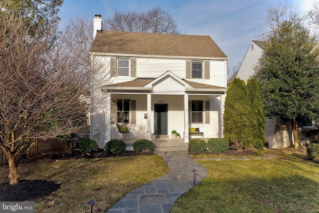 view of front of property featuring a front yard, fence, a porch, a chimney, and brick siding