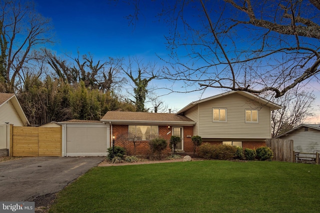 split level home featuring brick siding, an attached garage, fence, a front yard, and driveway