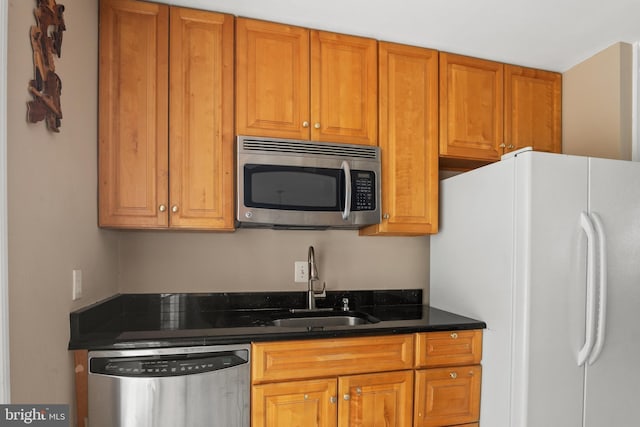 kitchen with dark countertops, brown cabinets, appliances with stainless steel finishes, and a sink