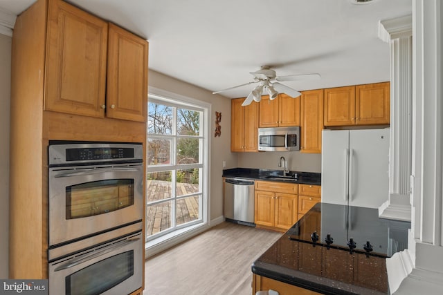 kitchen with light wood-style flooring, a sink, dark stone countertops, appliances with stainless steel finishes, and ceiling fan