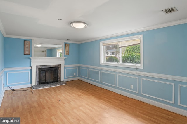 unfurnished living room featuring visible vents, a brick fireplace, ornamental molding, wood finished floors, and a decorative wall