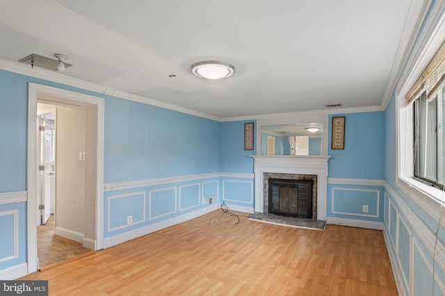 unfurnished living room featuring visible vents, ornamental molding, a fireplace, wood finished floors, and a decorative wall