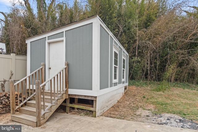 view of outbuilding with entry steps, an outbuilding, and fence