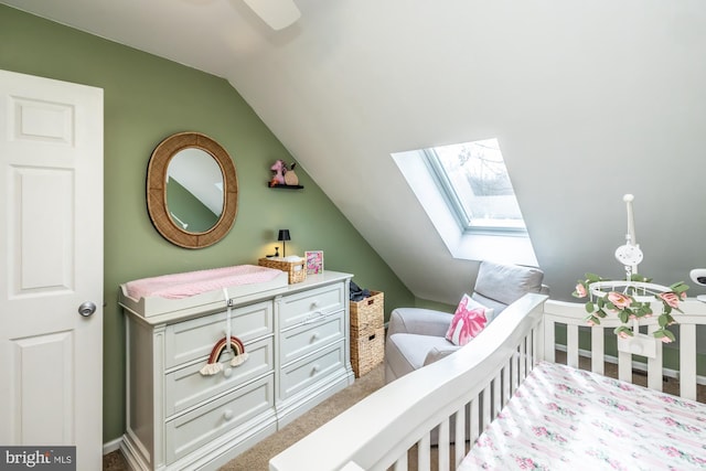 carpeted bedroom featuring a crib, lofted ceiling with skylight, and baseboards