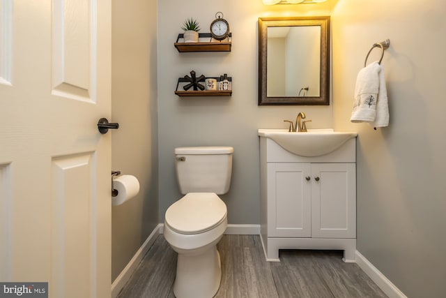 bathroom with vanity, toilet, wood finished floors, and baseboards