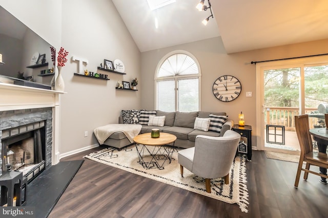 living room with wood finished floors, baseboards, a fireplace with raised hearth, vaulted ceiling, and track lighting