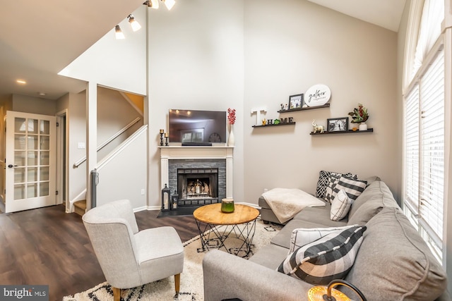 living area featuring a wealth of natural light, a fireplace with flush hearth, a towering ceiling, and wood finished floors