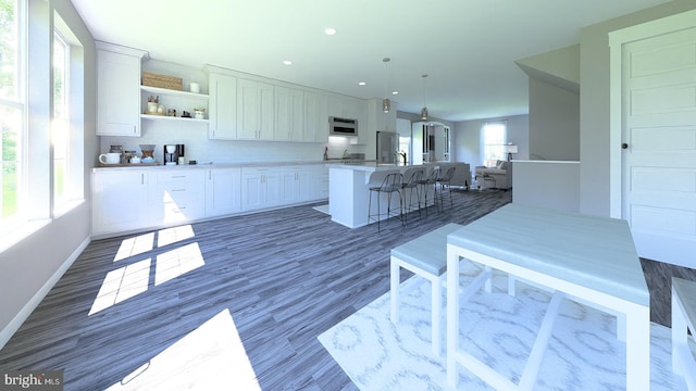 kitchen featuring open shelves, a kitchen bar, a center island with sink, and white cabinetry