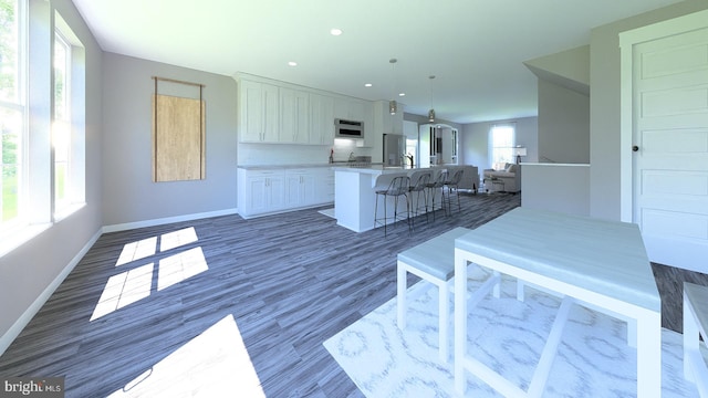 kitchen featuring a breakfast bar area, baseboards, an island with sink, light countertops, and white cabinets