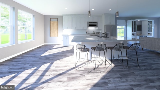 kitchen featuring a center island with sink, arched walkways, a sink, a kitchen breakfast bar, and stainless steel fridge