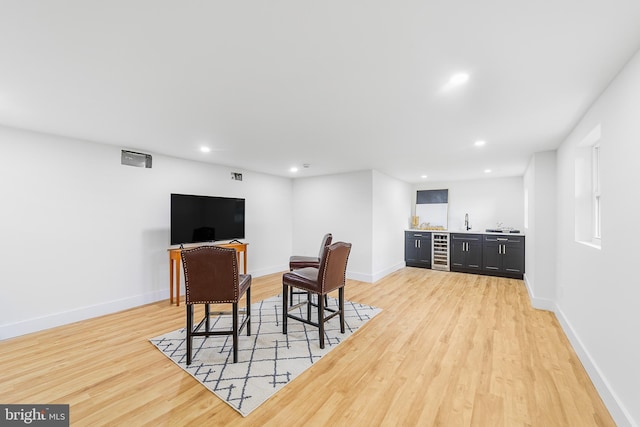 interior space featuring beverage cooler, indoor wet bar, light wood-type flooring, and baseboards