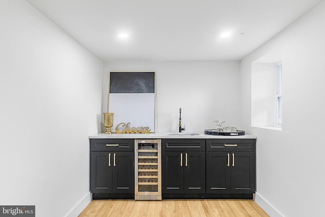 bar with baseboards, wine cooler, indoor wet bar, light wood-style flooring, and a sink