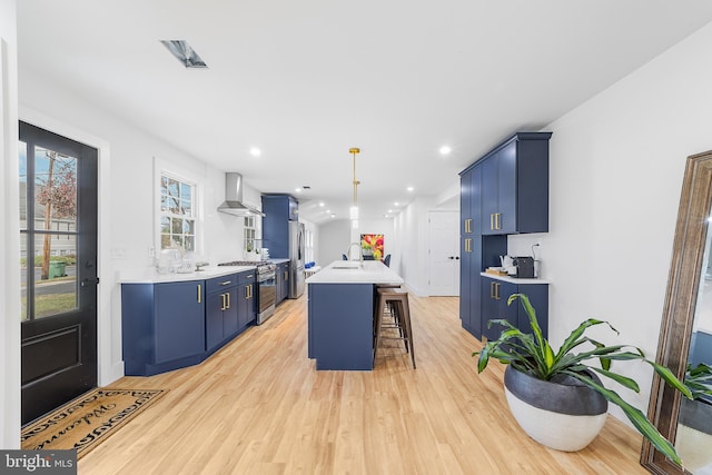 kitchen featuring wall chimney range hood, a kitchen bar, appliances with stainless steel finishes, blue cabinets, and a sink