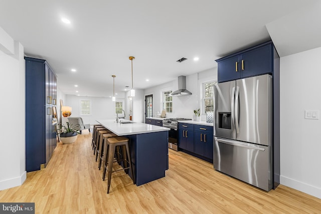 kitchen with blue cabinets, a sink, appliances with stainless steel finishes, wall chimney exhaust hood, and light countertops