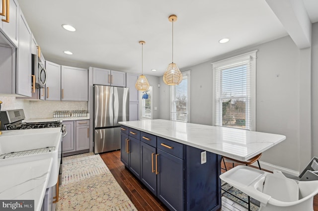 kitchen with dark wood-type flooring, light stone counters, blue cabinetry, backsplash, and appliances with stainless steel finishes