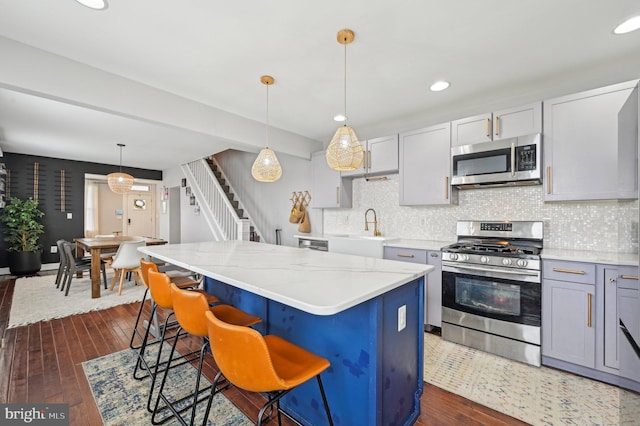 kitchen with a center island, dark wood-type flooring, light stone countertops, appliances with stainless steel finishes, and a sink