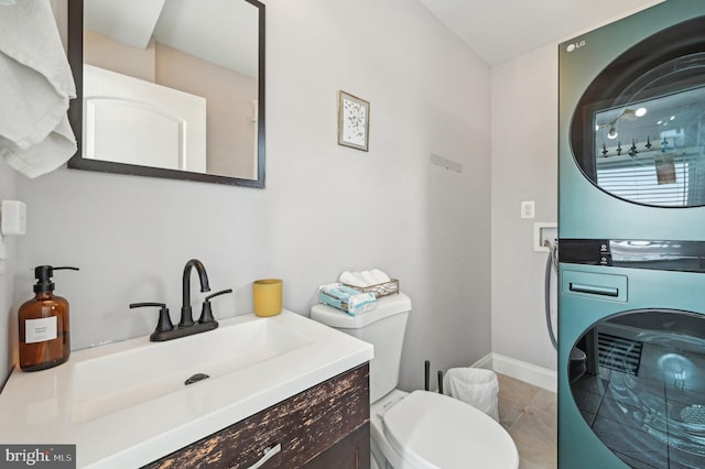 bathroom with baseboards, toilet, stacked washing maching and dryer, tile patterned floors, and vanity