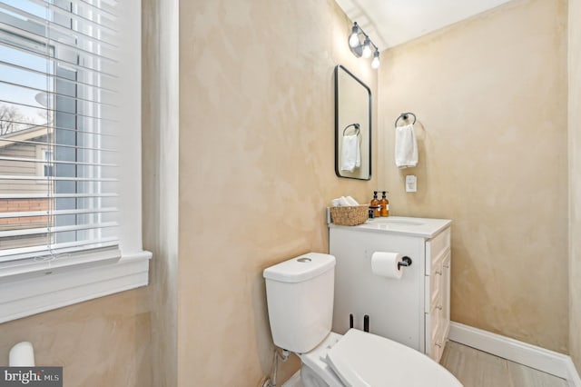 half bathroom featuring vanity, toilet, and baseboards