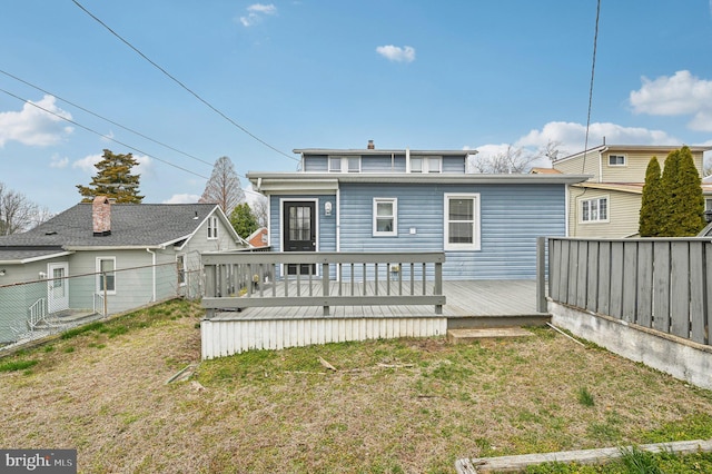 back of property with a wooden deck, a lawn, and fence