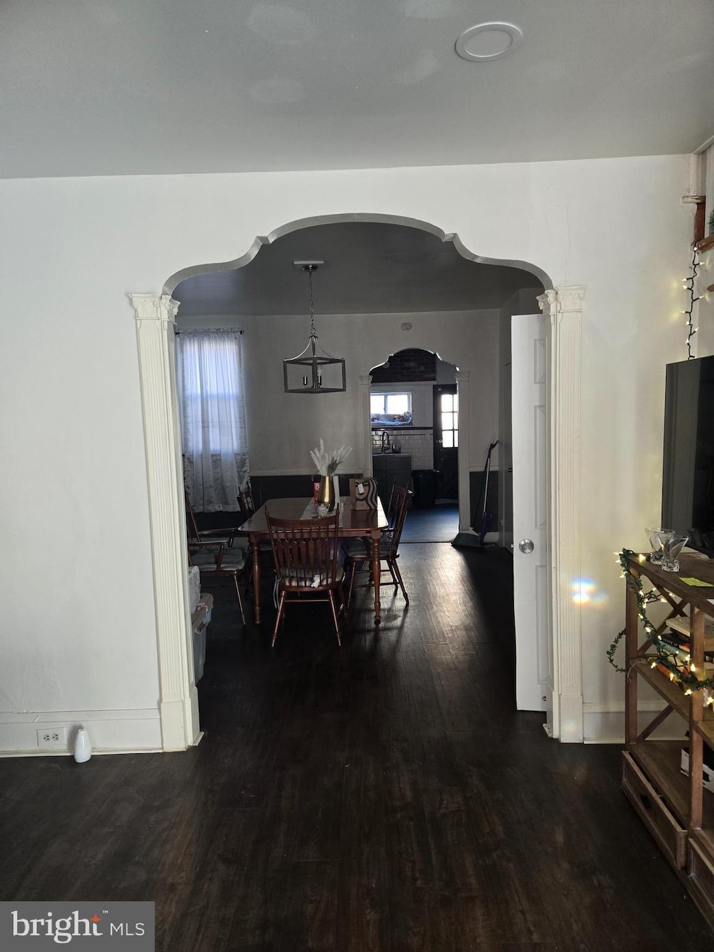 dining space featuring baseboards, arched walkways, dark wood-type flooring, and ornate columns