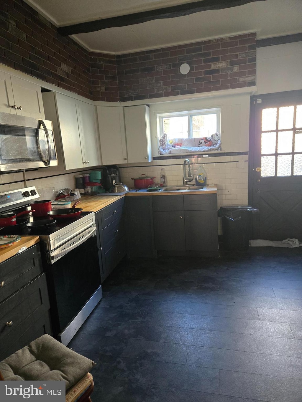 kitchen featuring brick wall, a sink, stainless steel appliances, light countertops, and white cabinets