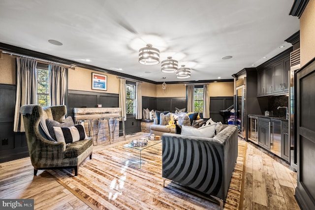 living area featuring a decorative wall, light wood-style floors, wainscoting, and crown molding