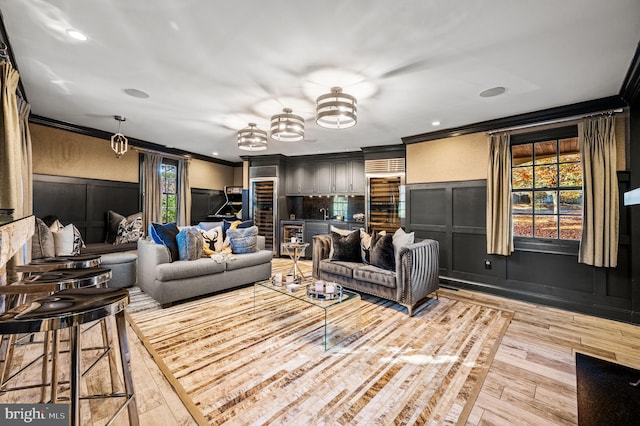 living area with wine cooler, light wood-style flooring, crown molding, and a decorative wall