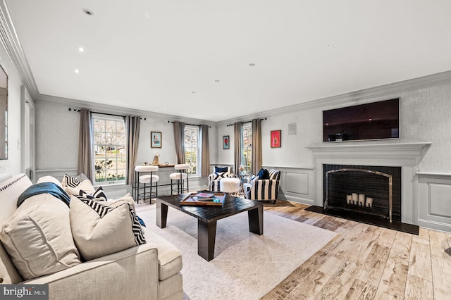 living area featuring crown molding, a fireplace with flush hearth, and wainscoting